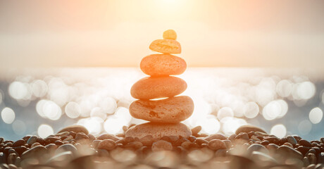 Balanced pebbles pyramid on the beach on sunny day and clear sky at sunset. Blue sea on background. Selective focus, bokeh. Zen stones on sea beach, meditation, spa, harmony, calm, balance concept