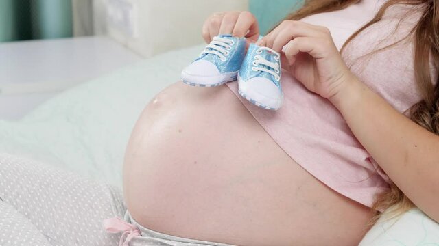 CLoseup of pregnant woman lying in bed and dancing with baby boots on big belly. Concept of pregnancy and expecting baby
