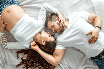 Pregnant girl with her husband lie on white sheets. Beautiful belly of a young attractive pregnant girl. Family, marriage, childbirth concept.