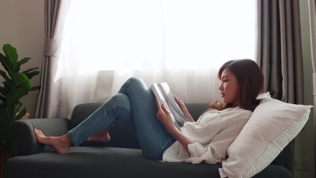Lovely Asian women lie on the sofa, read magazines in their spare time, and relax in the mornings in the living room in the house.
