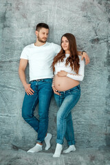 A pregnant girl and her husband are standing against the wall. Beautiful belly of a young attractive pregnant girl. Family, marriage, childbirth concept.