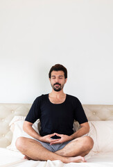 Man with mustache meditating while sitting on bed in morning. Young man doing yoga in bed. Male meditating on bed at home. Meditate on the bed before sleep.