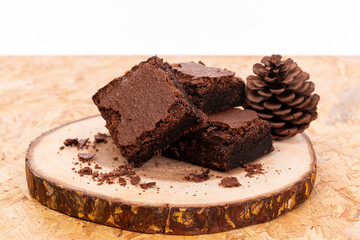 Pieces of fresh chocolate brownie on wooden plate on white background. Stack of fudgy chocolate brownies on white background, homemade bakery and dessert. Brownie chewy squares stack on wooden plate.