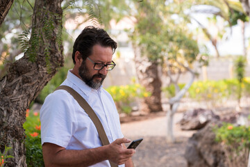 Fototapeta premium Portrait of adult caucasian man use mobile cellular smart phone outdoor at the park - modern people and connection technology - search the web with free wifi internet signal