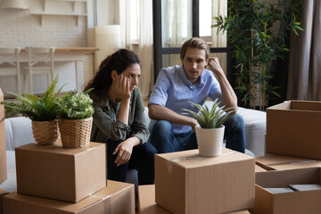 Unhappy young Caucasian man and woman sit on couch argue quarrel on moving day to new home....