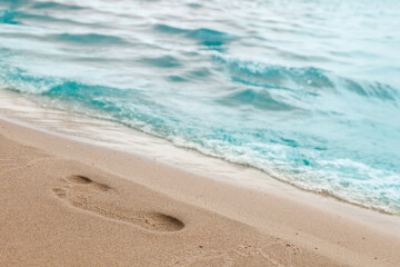 Close-up of the beach shore with a man's footprint on the yellow sand along the line of the blue sea wave on a summer sunny day. Background for advertising travel or tourist vacation.