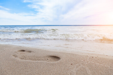 Close-up of the beach shore with a man's footprint on the yellow sand along the line of the blue sea wave on a summer sunny day. Background for advertising travel or tourist vacation.