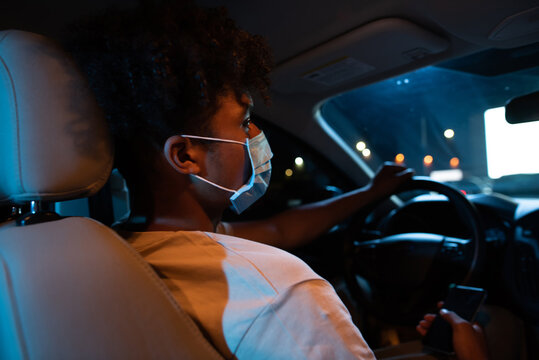 Close up of young guy, male driver wearing protective mask while sitting in front seat of the car