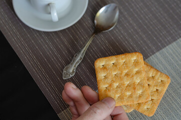 Fragment of man's hand holding square cracker in his hand above table.