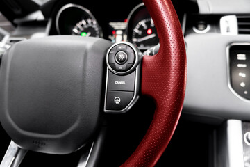 Cruise control buttons on the red perforated leather steering wheel of a modern car.  Car interior...