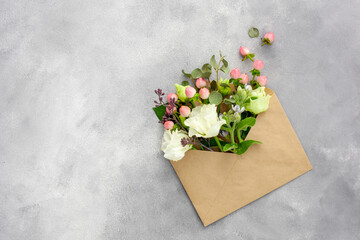 Fototapeta na wymiar Postcard with open kraft paper envelope filled with spring flowers
