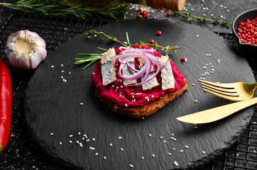 Sandwich with beet hummus, herring and onions. Breakfast. On a black stone plate.