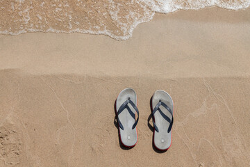 Fototapeta na wymiar A pair of sandals with red soles on a sunny beach with sand near the seashore on a summer day. Rest and travel to hot countries. Vacation.