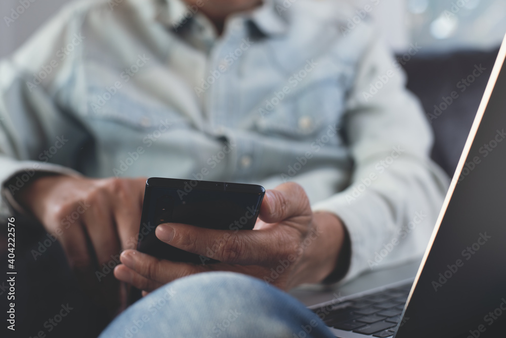 Wall mural man wearing casual clothes sitting on sofa using mobile phone for online shopping and internet banki