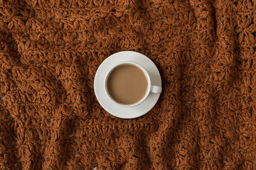 Cup of coffee with milk on dark brown crumpled knitted woolen textile cloth texture. Flatlay, top view.