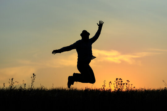 silhouette of a joyful adult man in a hat who jumps with happiness against the background of the evening sky