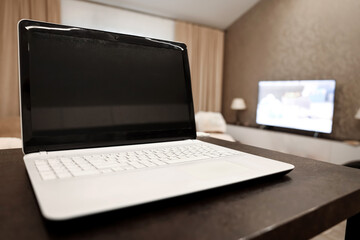 Fototapeta premium A laptop with a blank black screen in an angular position on a table against a blurred room background. The concept of workplace, office, coworking.
