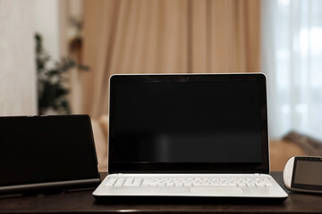 A laptop with a blank black screen in an angular position on a table against a blurred room background. The concept of workplace, office, coworking.