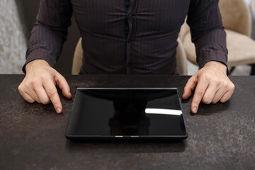 Black tablet with blank screen and male hands on the table, top view. Concept businessman, office, finance.