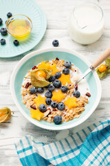 Healthy breakfast. Fresh granola, muesli with milk, honey and berries. White wooden background.
