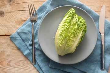 Fresh green lettuce or baby cos on a gray plate with cutlery on a blue napkin and rustic wooden...