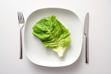 Green lettuce leaf on a square plate and cutlery on a white background, healthy diet to lose weight...