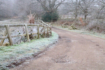 English country scene in winter showing icy lane with fencing and trees