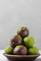 Homemade healthy matcha bliss energy balls in chocolate glaze with dates, coconut and nuts on gray background