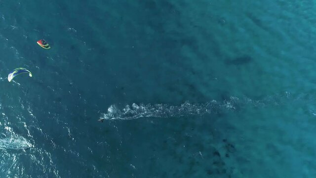 drone footage of people kitesurfing with their kites above turquoise water