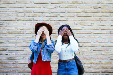 Two female friends covering their eyes outdoors. Multiethnic women.