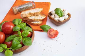 mozzarella and green basil in a wooden bowl, fresh tomatoes, near white bread croutons and spices on a table