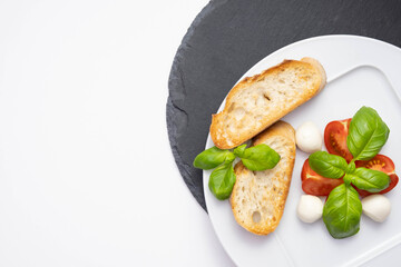 small mozzarella, fresh basil and chopped tomatoes on a white plate and on a stone stand white bread croutons