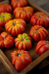 Red ribbed tomatoes on a wooden background. American or Florentine variety Nina. Food on the table top view. Autumn harvest of vegetables similar to flowers and pumpkins.Ribby tomato.