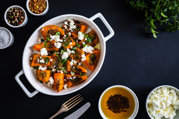 Roasted spicy pumpkin with feta cheese on black table 