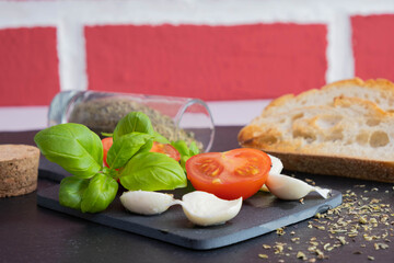 on a stone board lie tomatoes, basil and mozzarella next to crackers and spices