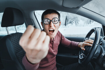 Funny and ridiculous nerd driver in eyeglasses shouting to the camera and showing his fist inside a...