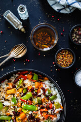 White rice with mix of vegetables in frying pan on black wooden table
