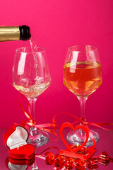Champagne is poured into glasses on a pink background next to a heart candlestick with a burning candle.