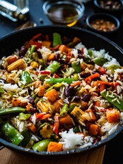 White rice with mix of vegetables in frying pan on black wooden table

