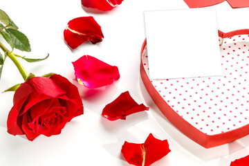 Postcard copy place in a box in the shape of a heart on a white background with a postcard in the middle of rose petals and next to a rose.