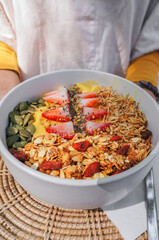 Close up Woman holding a pineapple and mango smoothie bowls with fruits, fresh Strawberry, nuts, seeds and homemade granola for healthy vegan