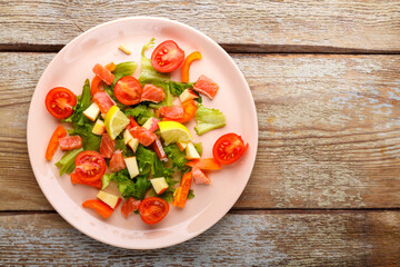 Salad with salmon and cherry tomatoes and green salad in a plate on a wooden table. Copy space