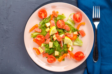 Salad with salmon and cherry tomatoes in a plate on a concrete background on a blue napkin next to a fork.