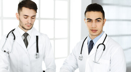 Arab doctor man sitting at the glass desk with caucasian colleague in medical office or clinic. Diverse doctors team, medicine and healthcare concept