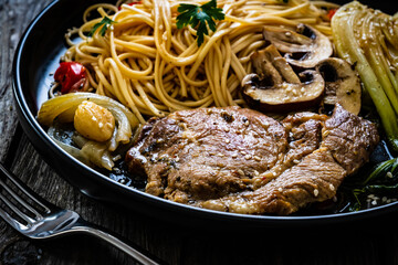 Fried pork steaks with mushrooms, noodles and steamed pak choi cabbage served on wooden table
