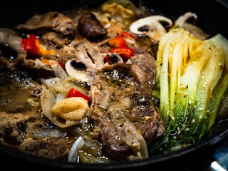 Pork steaks with mushrooms and pak choi cabbage frying in cooking pan 
