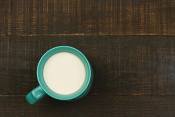 Green cup of milk on wooden background. Top view.