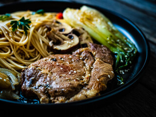 Fried pork steaks with mushrooms, noodles and steamed pak choi cabbage served on wooden table
