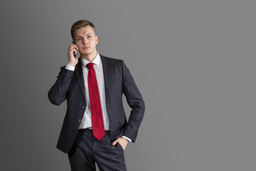 young handsome, attractive blond man in suit and red tie talking on the phone, smartphone. sad confident, serious businessman, lawyer on grey background. business concept. text.