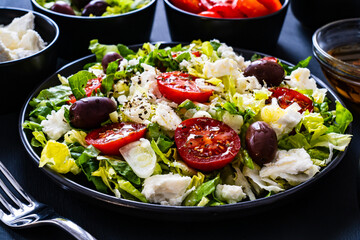 Fresh Greek salad - feta cheese, tomatoes, cucumber, lettuce, black olives and onion on wooden table
